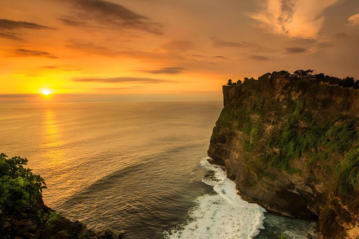 matahari terbenam di atas laut di samping tebing
