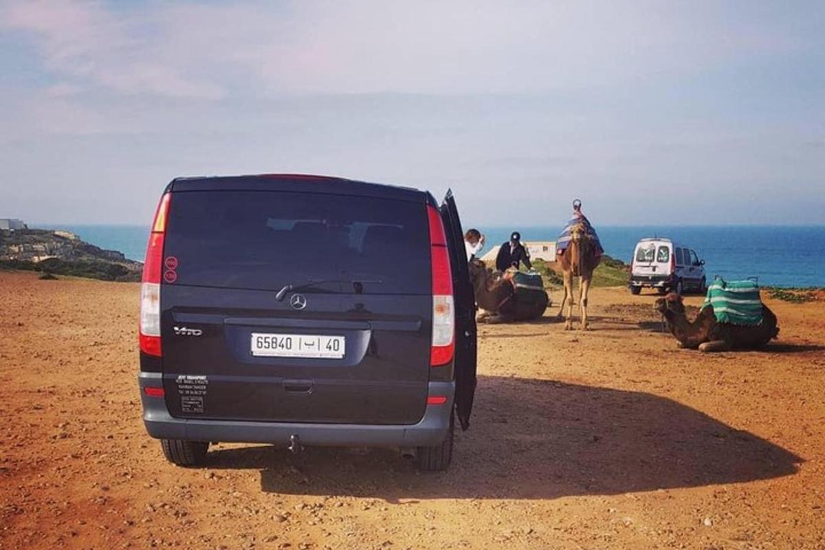 sebuah van hitam diletakkan di pantai dengan orang ramai dan seekor unta