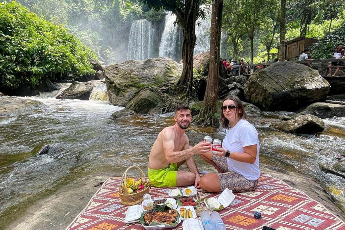 muž a žena sedící na piknikové dece před vodopádem