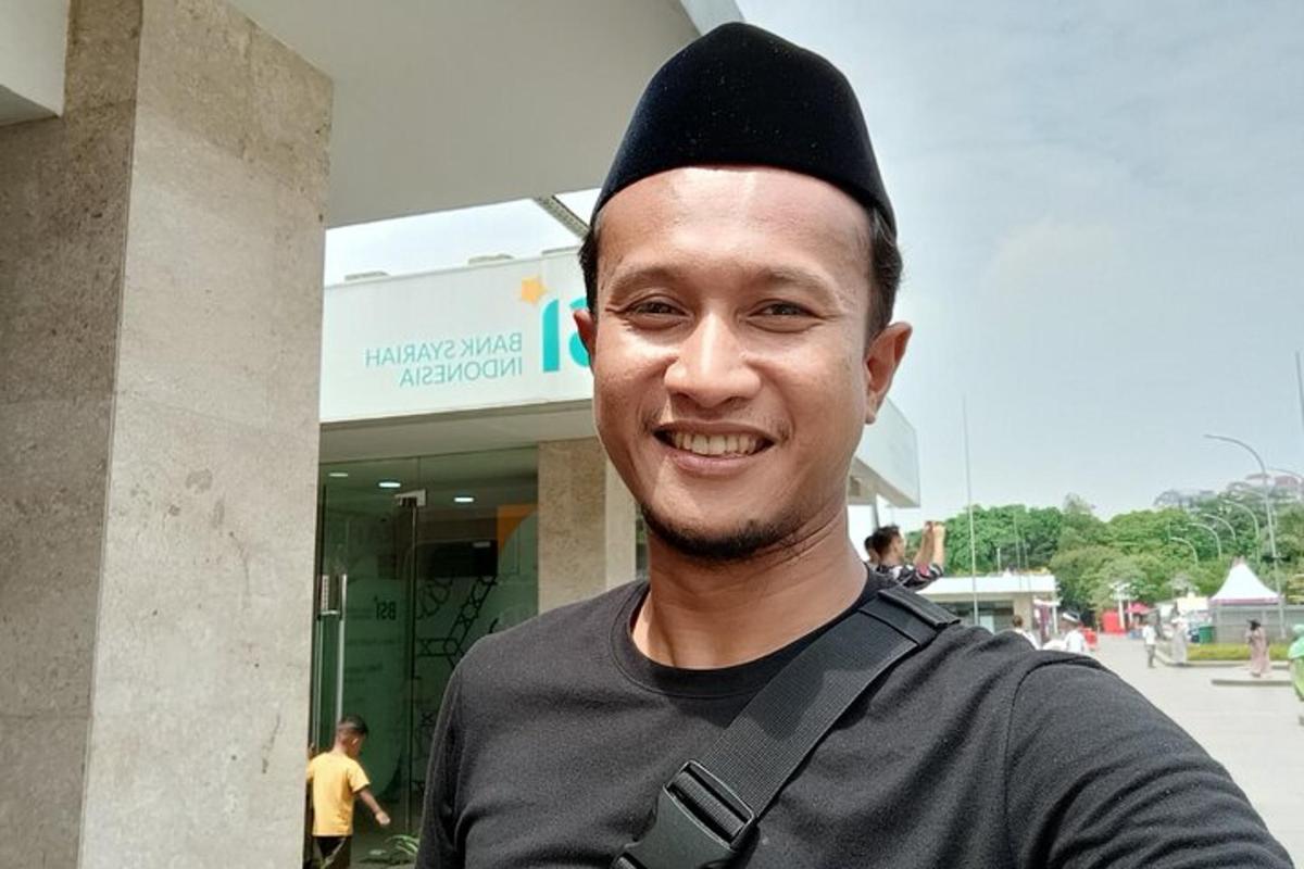 seorang lelaki memakai topi hitam berdiri di hadapan sebuah bangunan