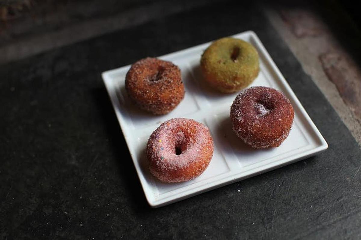 Cuatro donas en un plato blanco sobre una mesa.