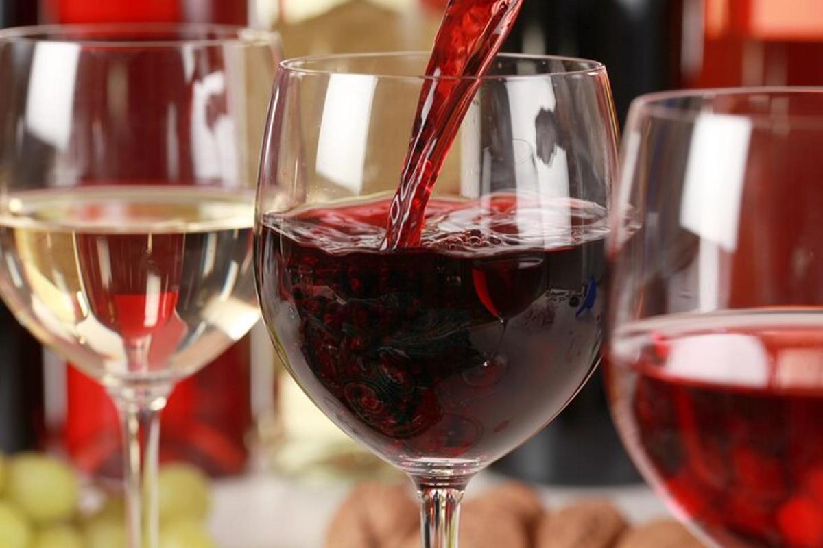 oseba, ki nalije rdeče vino v dva kozarca za vino