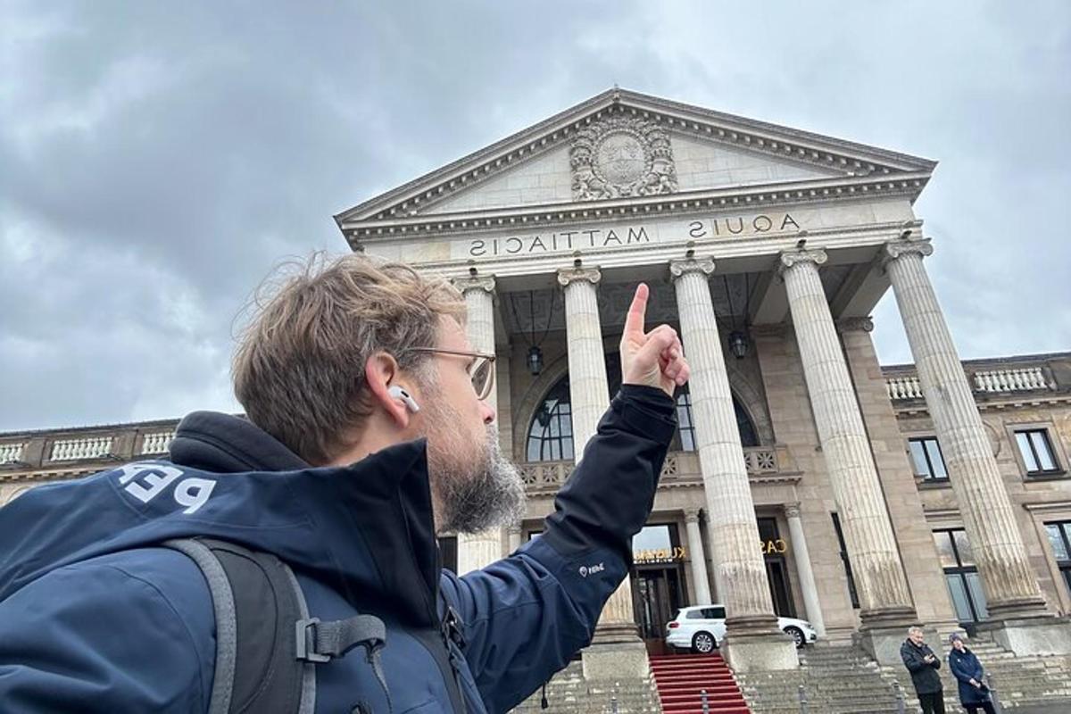 vīrietis ēkas priekšā rāda miera zīmi