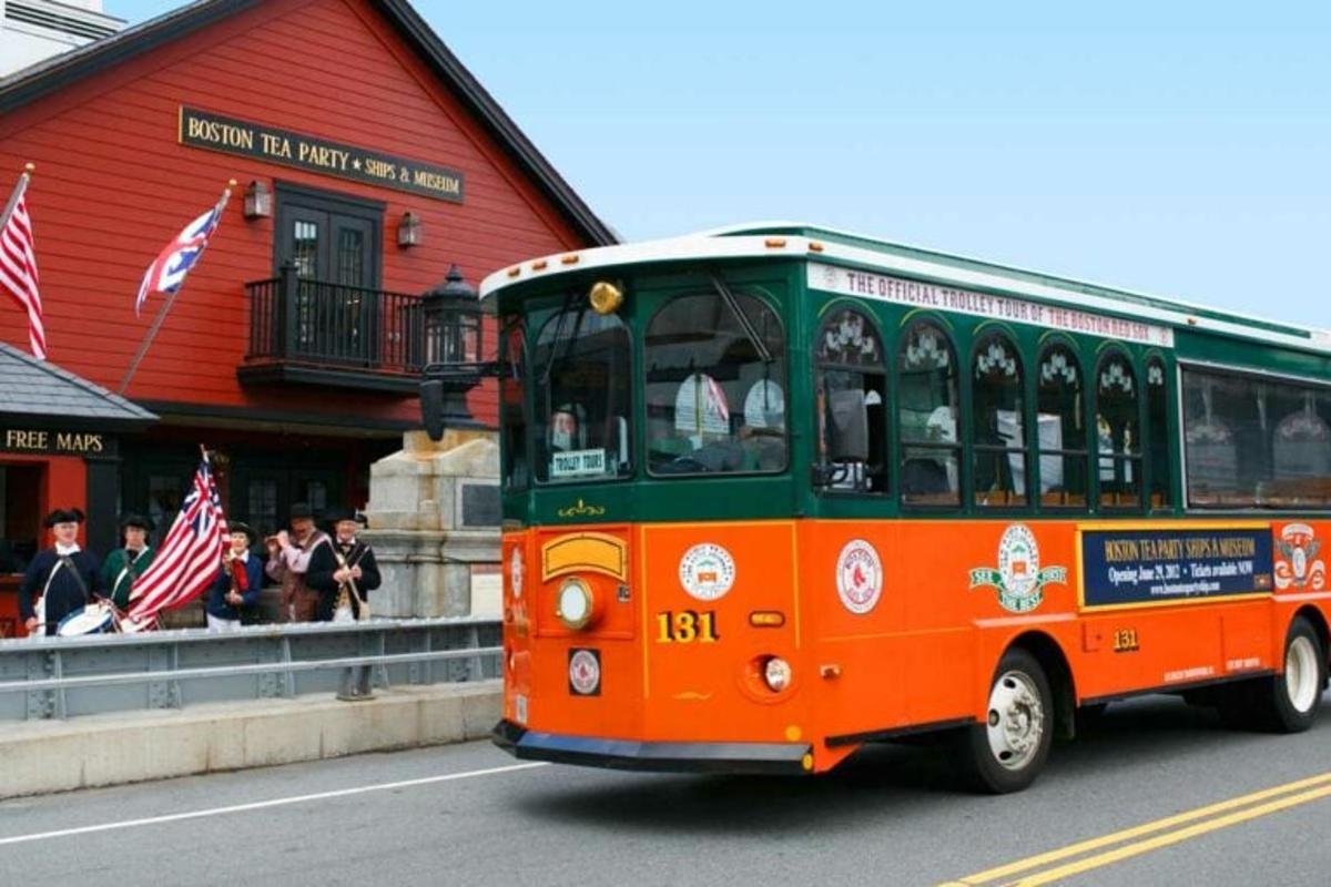 an orange and green bus driving past a red building