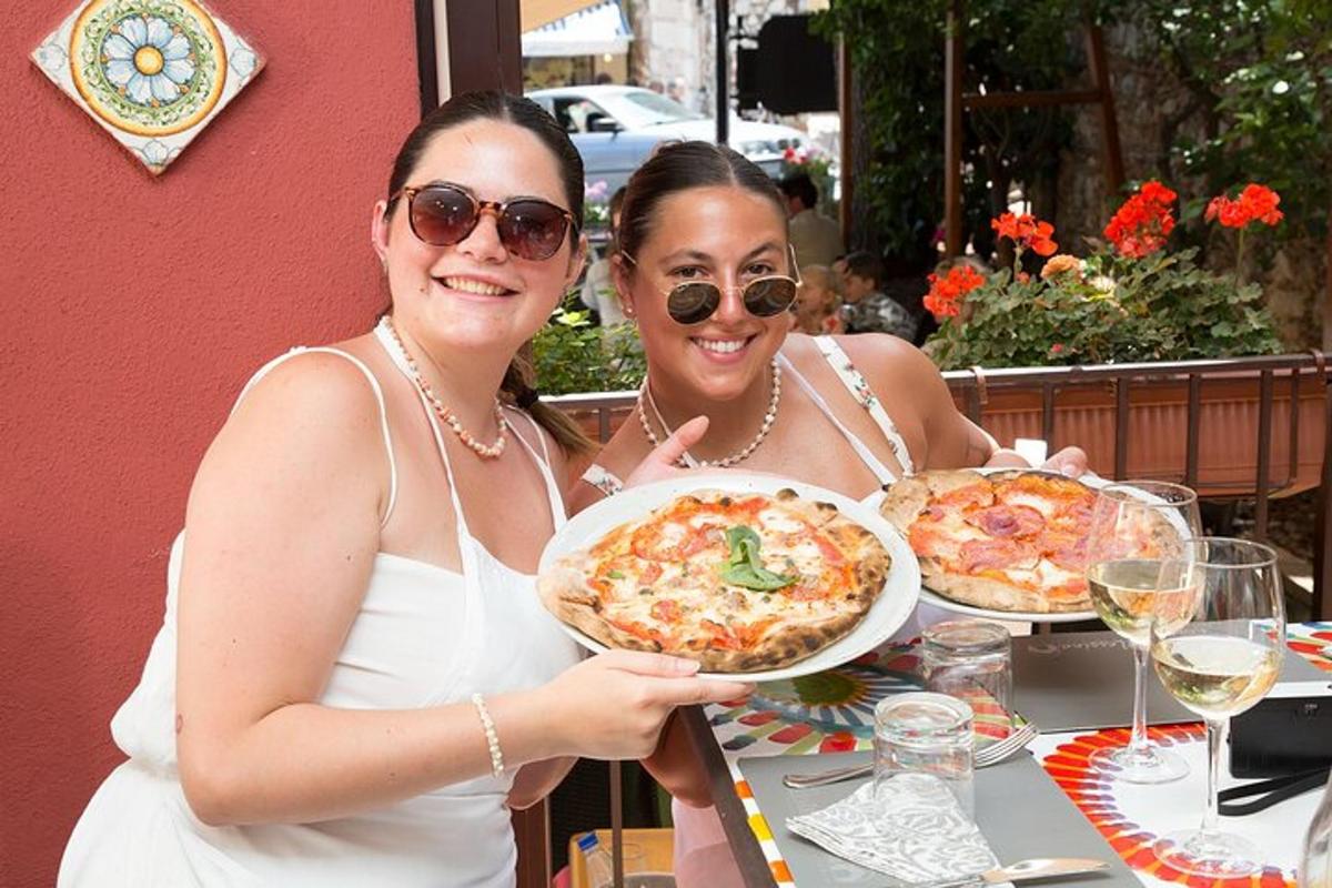 kaksi naista istuu pöydän ääressä ja pitelee pizzalautasta