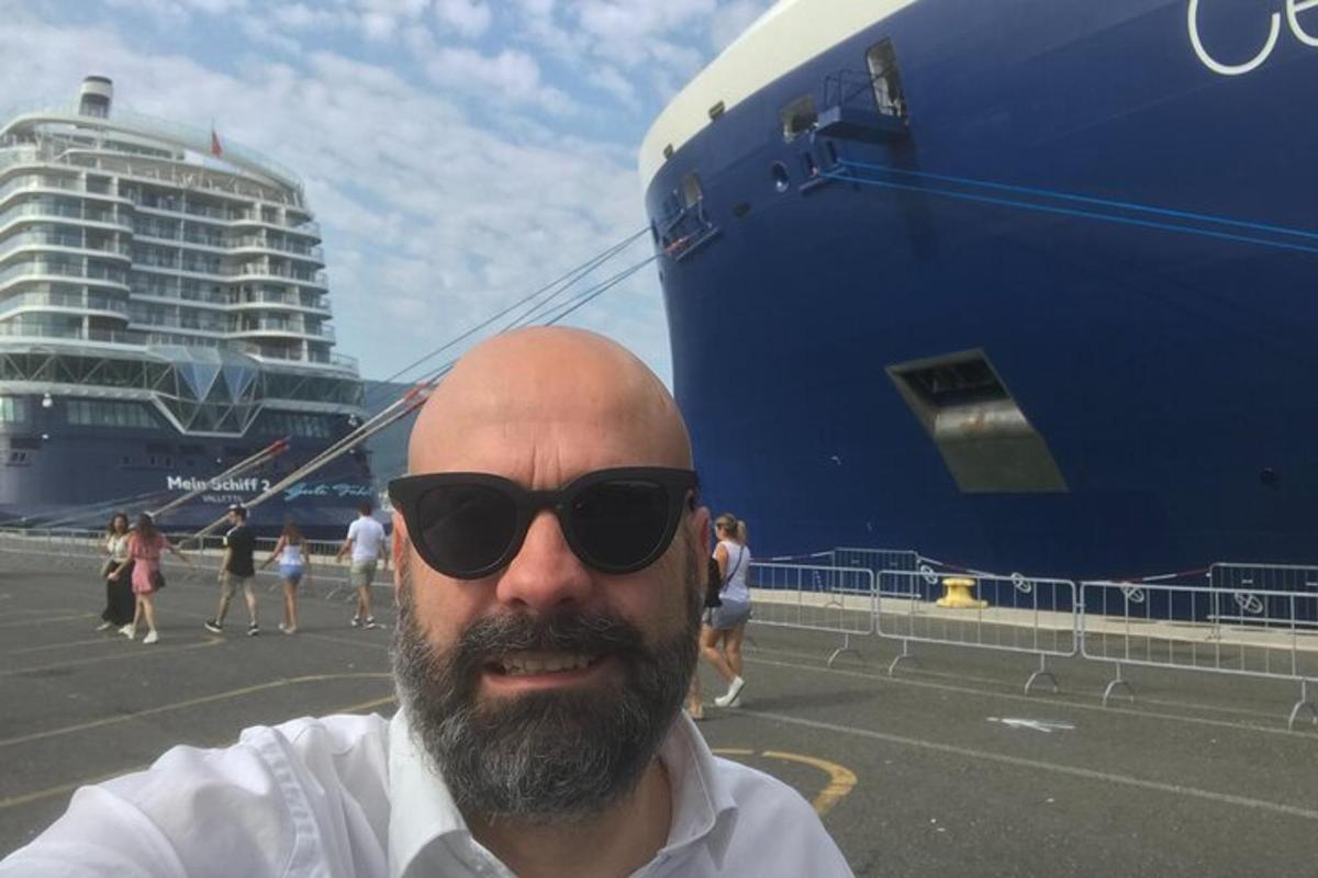 um homem usando óculos de sol em pé ao lado de um navio de cruzeiro