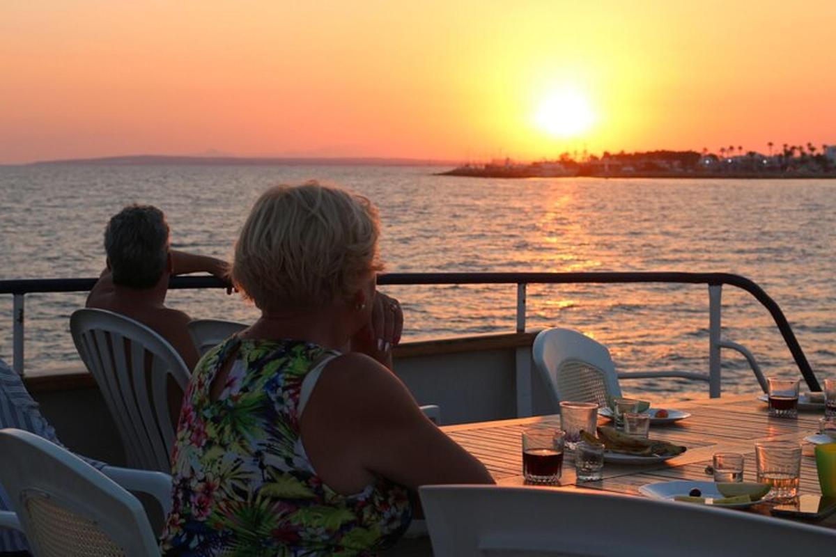 zwei Personen sitzen an einem Tisch auf einem Boot und beobachten den Sonnenuntergang