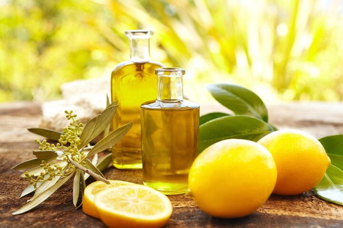 Una botella de aceite esencial de limón y limones sobre una mesa.