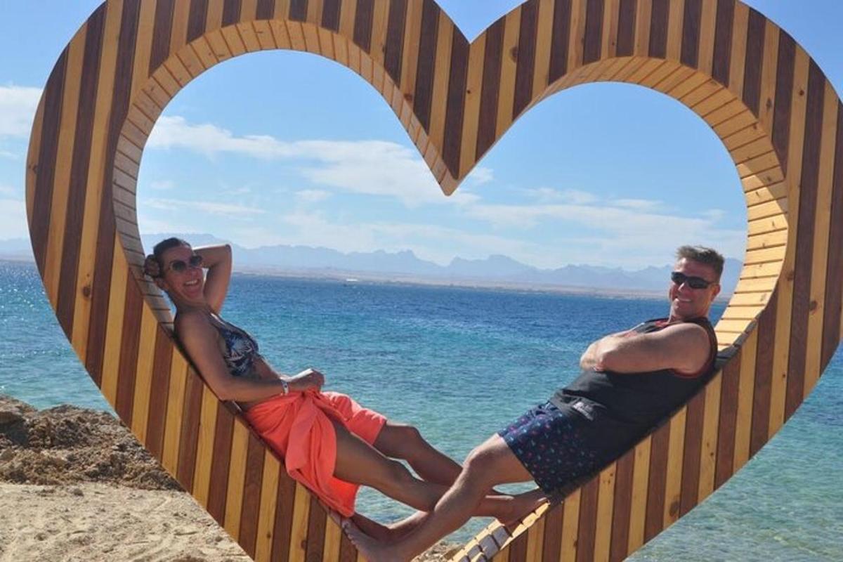 Muž a žena sedící na prkně ve tvaru srdce na pláži