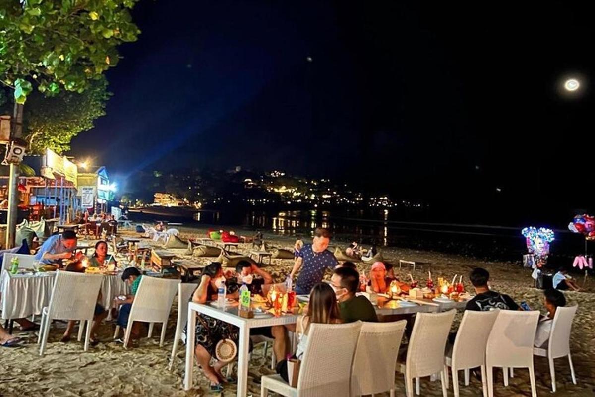 skupina ljudi, ki ponoči sedijo za mizami na plaži