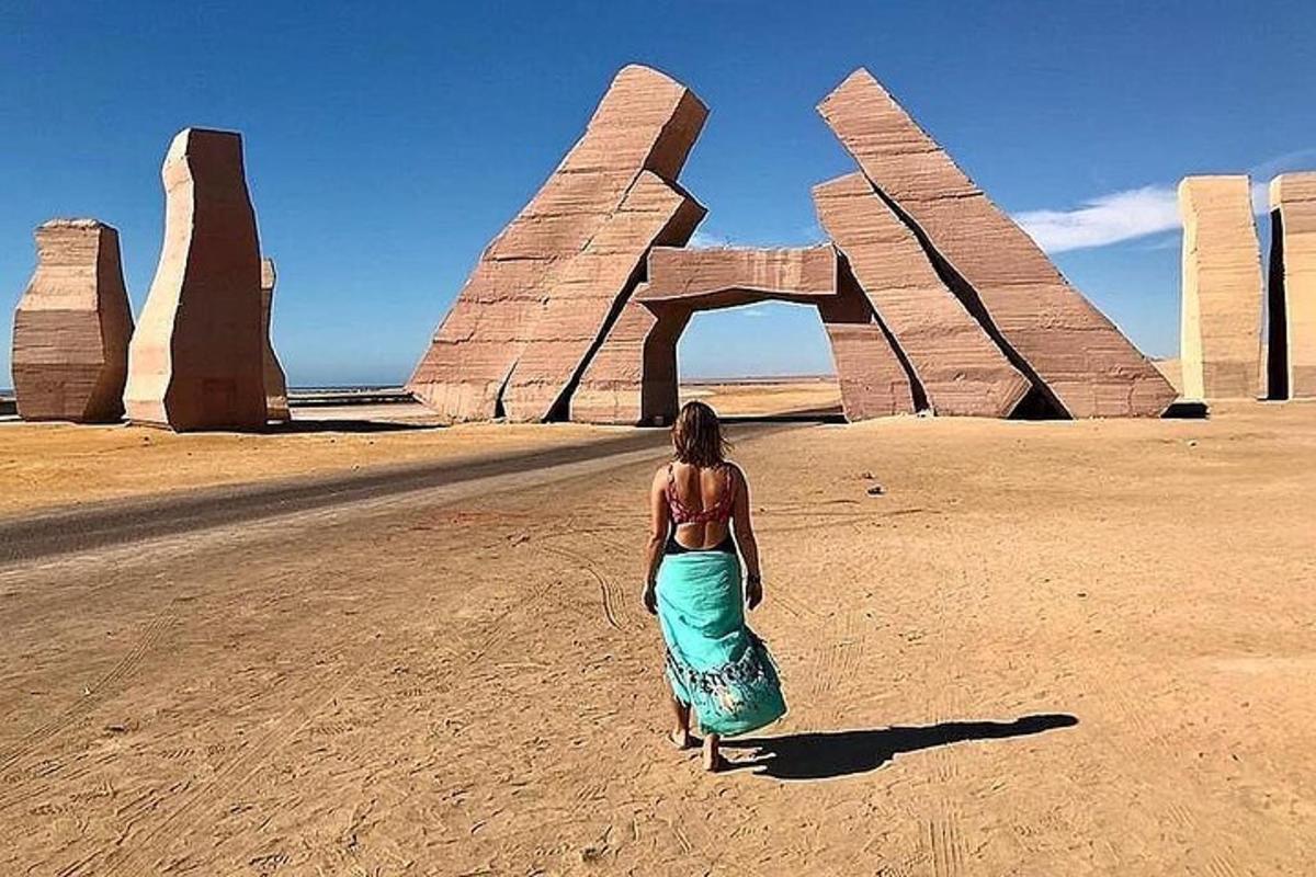 Una mujer parada frente a una escultura en el desierto.