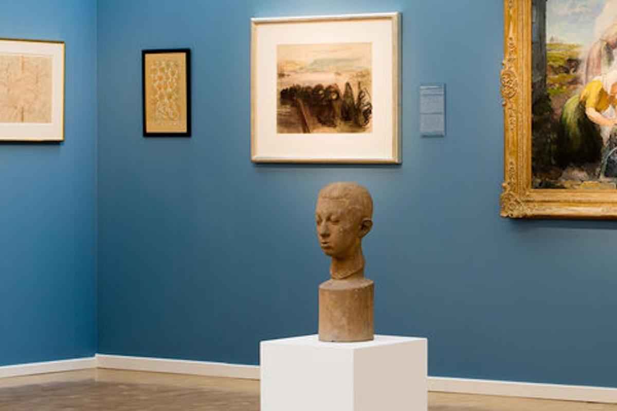 Un busto expuesto delante de pinturas en un museo.