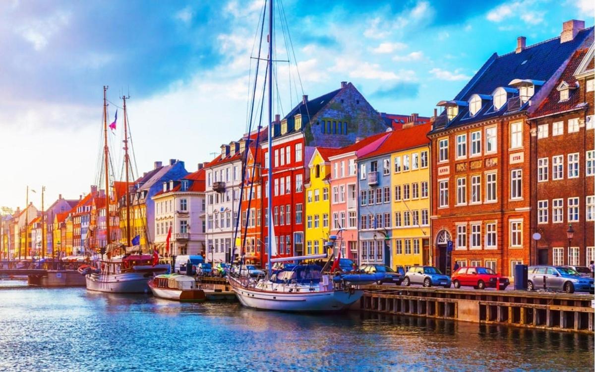 Hópur báta liggur að bryggju í á með byggingum