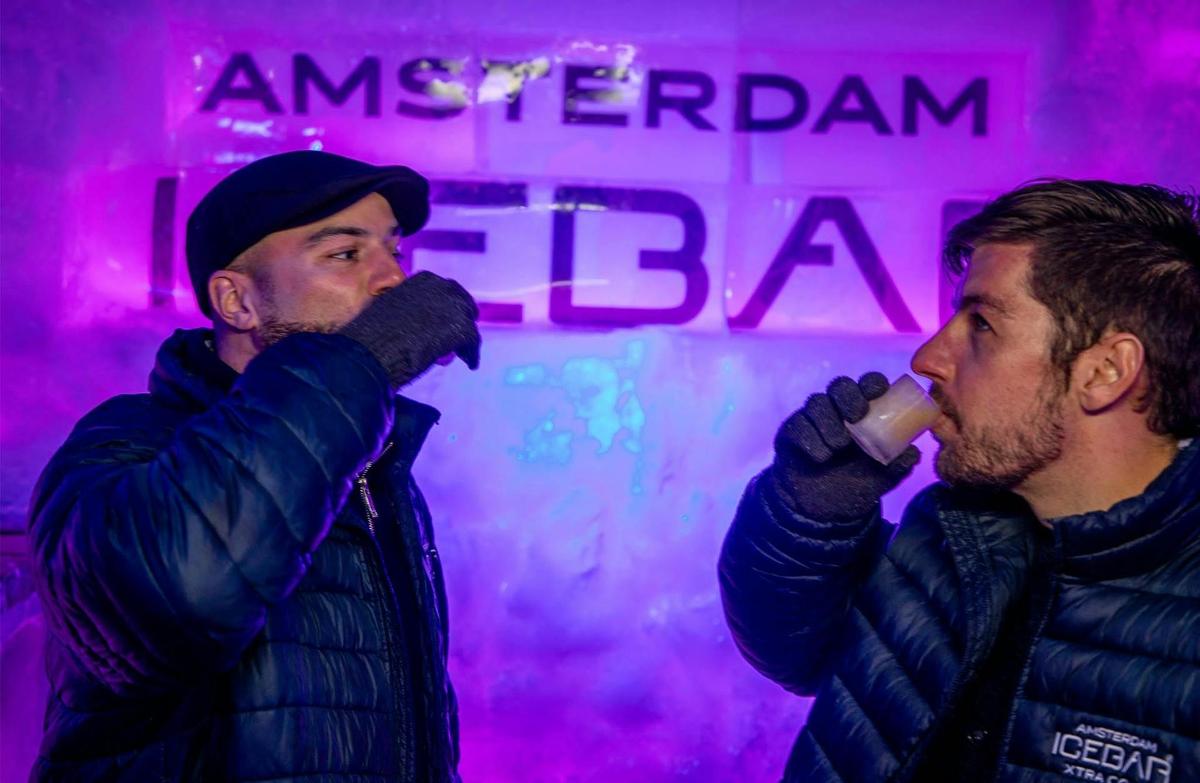 two men standing next to each other drinking