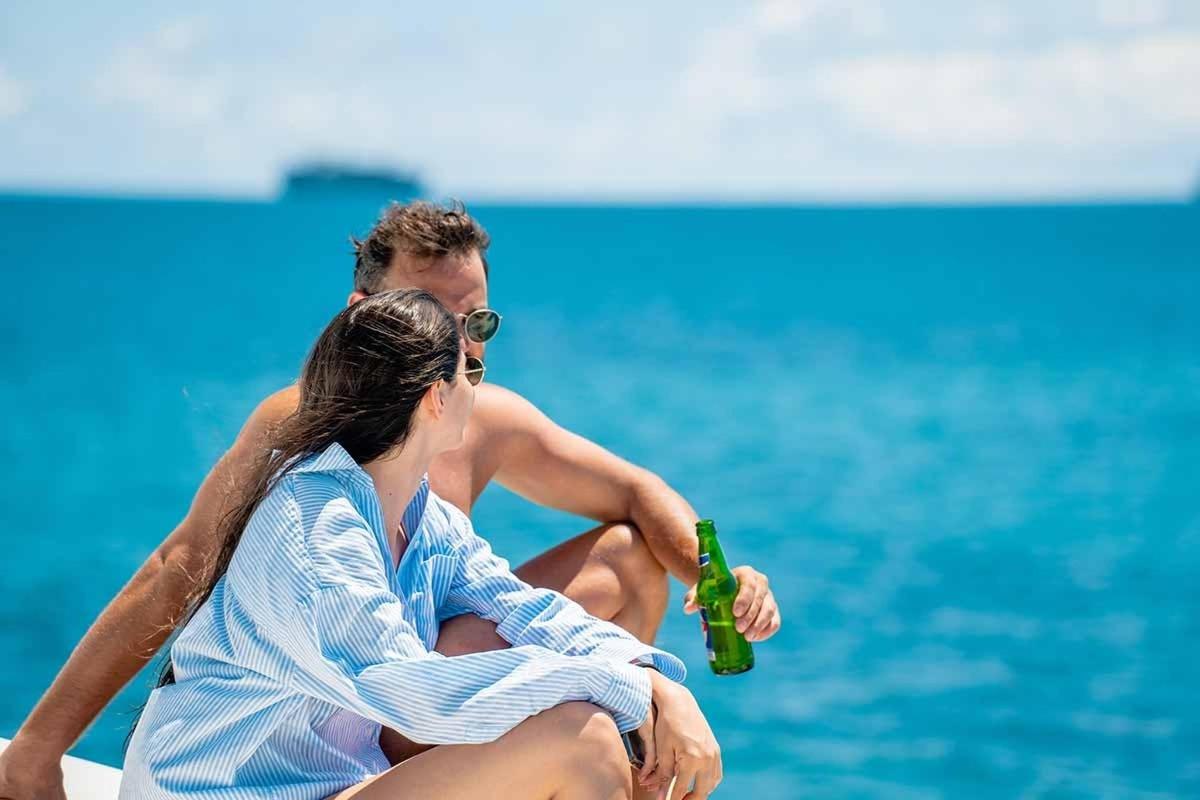a man and woman sitting next to the water with a beer