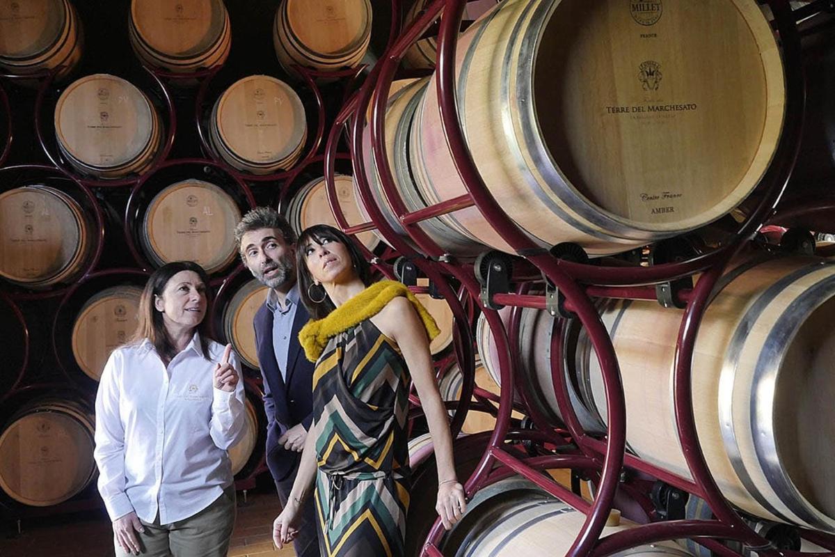 tre persone in piedi davanti a un mucchio di botti di vino