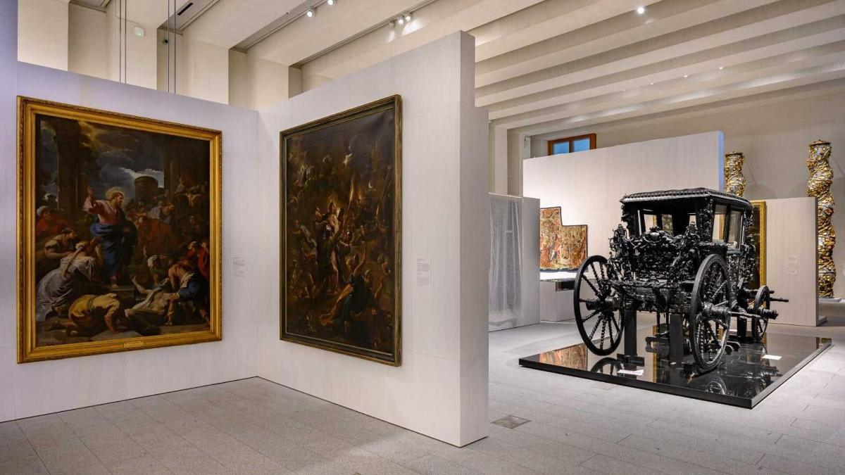 una sala museale con dipinti e una carrozza in mostra