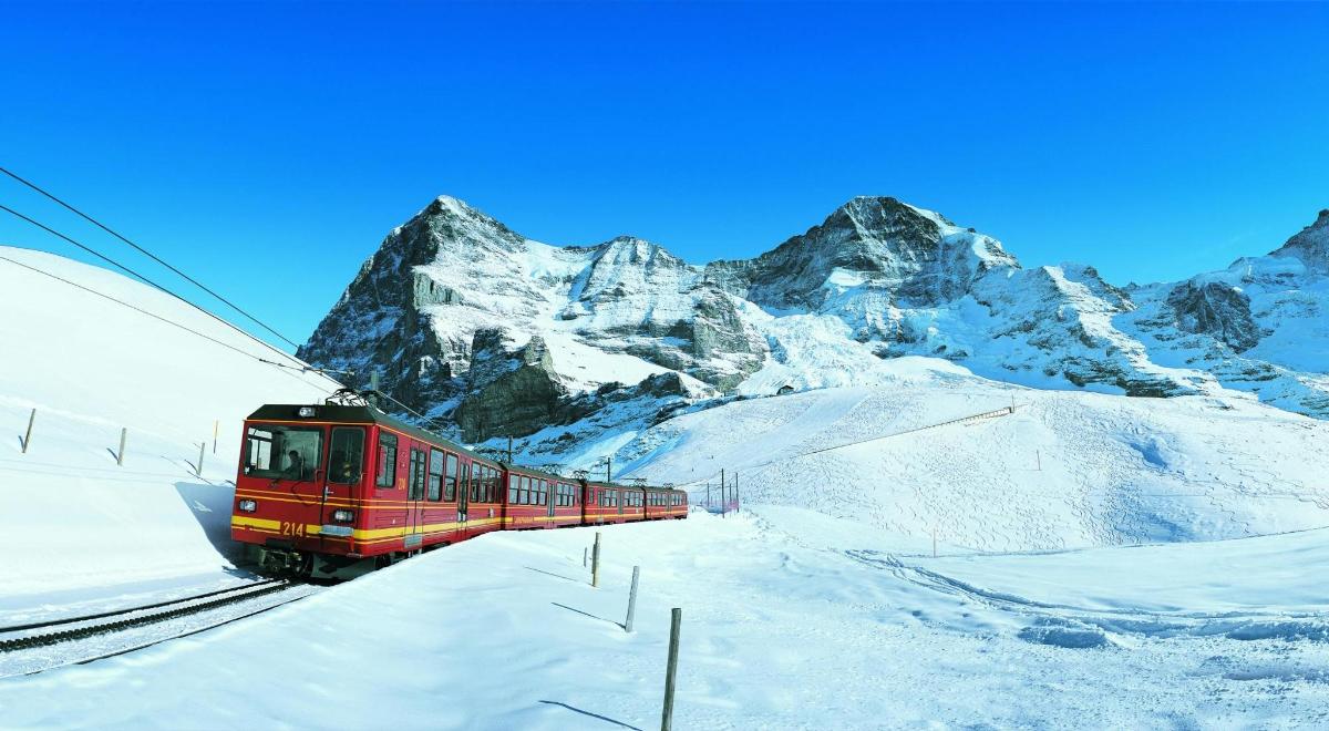 a red train on the tracks near a snow covered mountain
