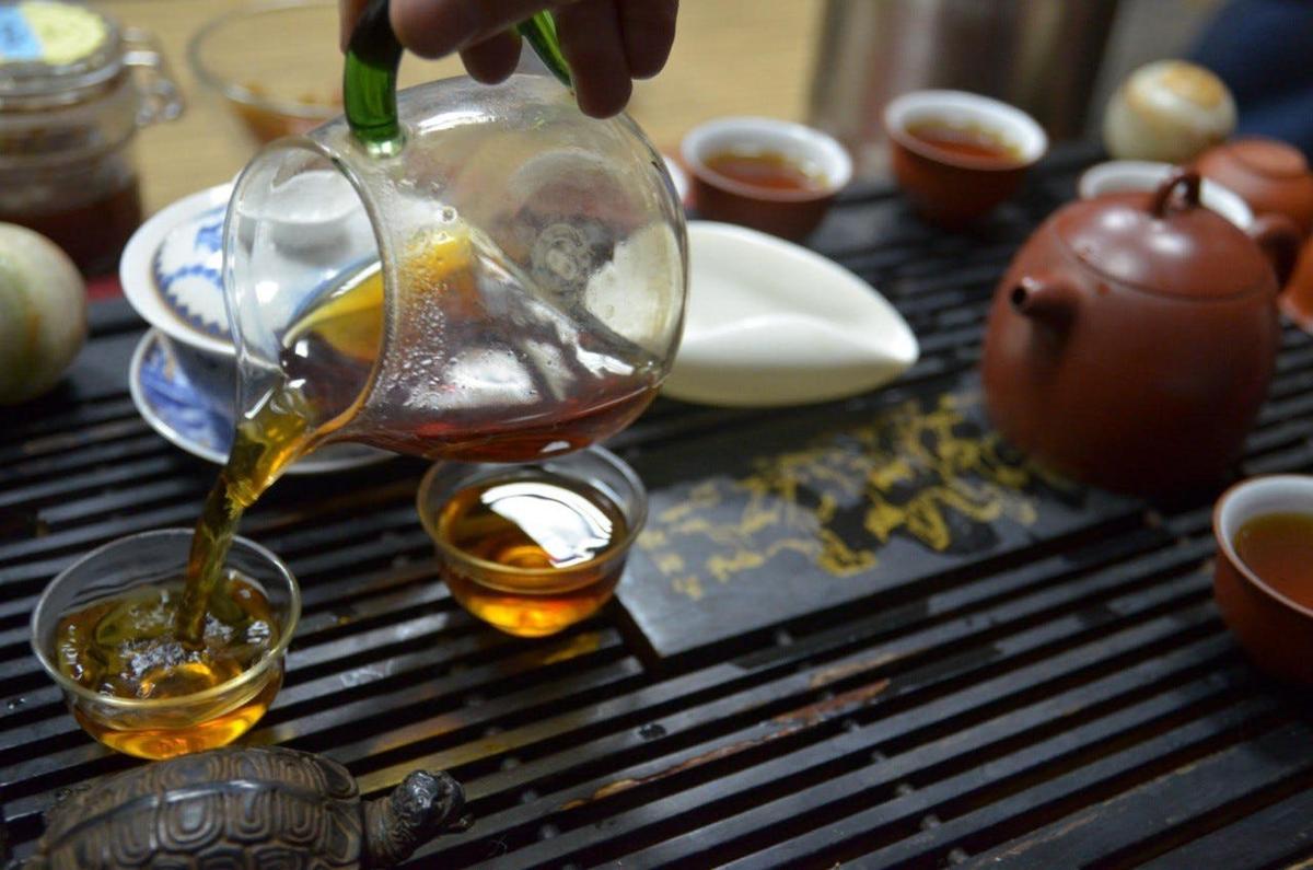 một người đang đổ dầu vào ấm trà trên bàn