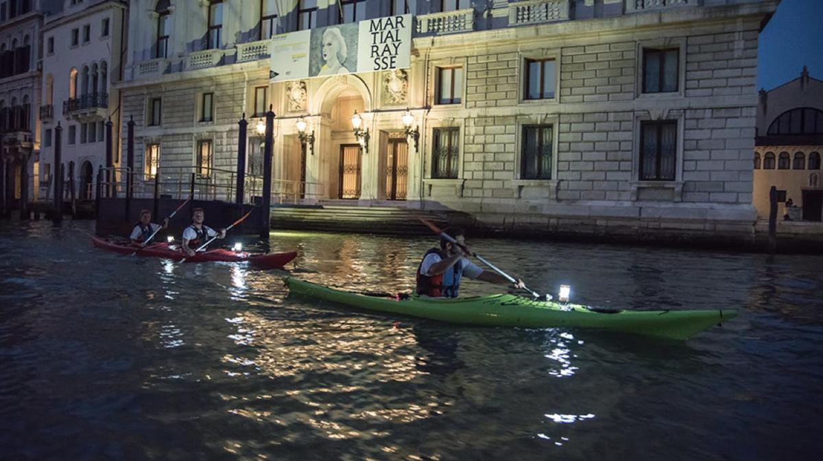 un gruppo di persone in canoa su un fiume di fronte a un edificio