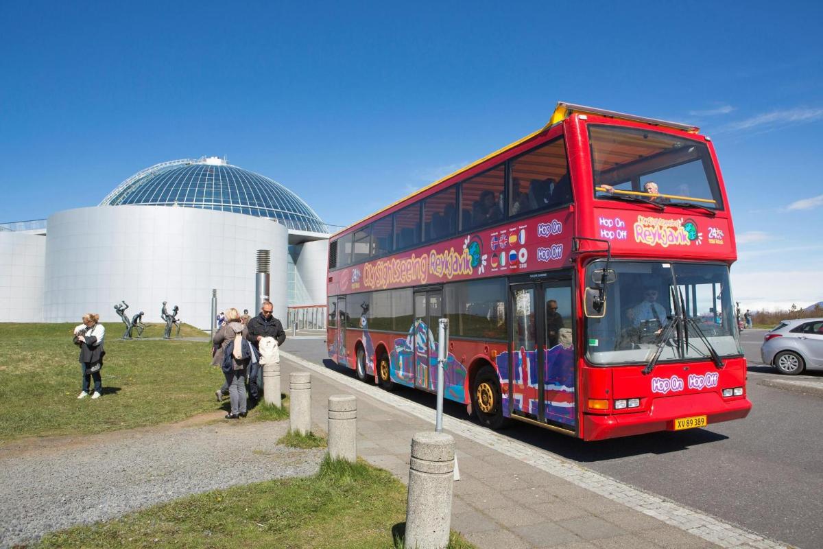 a red double decker bus driving past a building