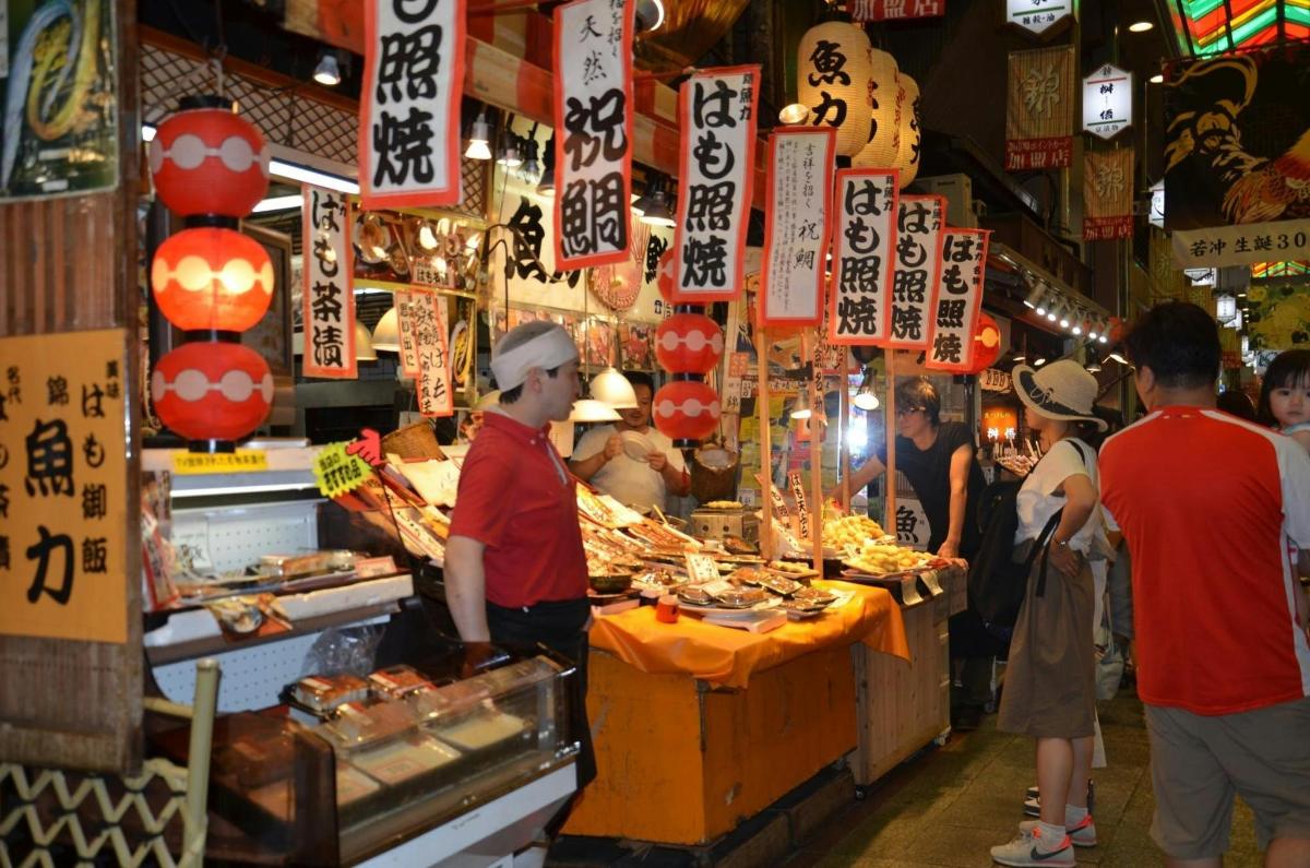 a group of people standing around a food stand in a market