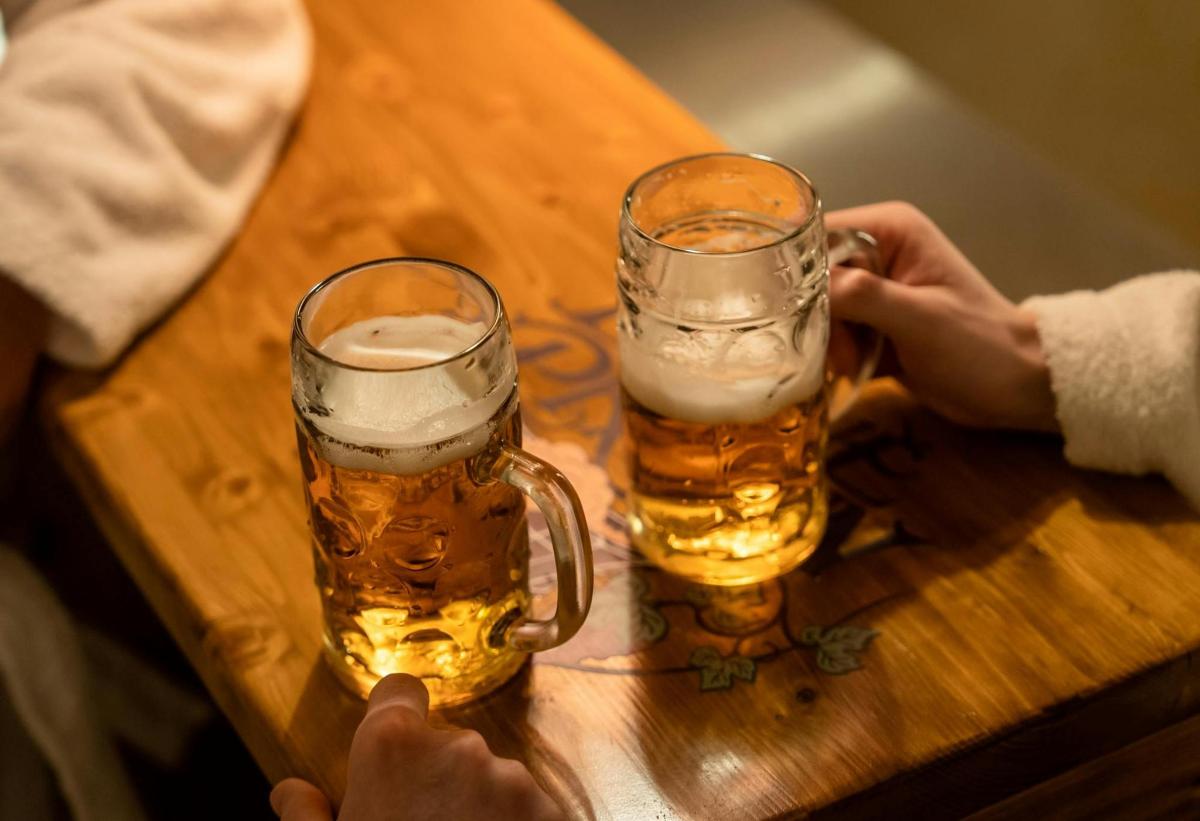 two people holding glasses of beer on a wooden table