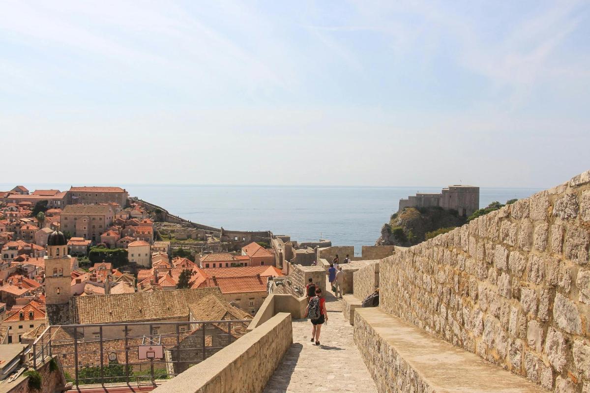 a woman walking along a wall looking at the ocean