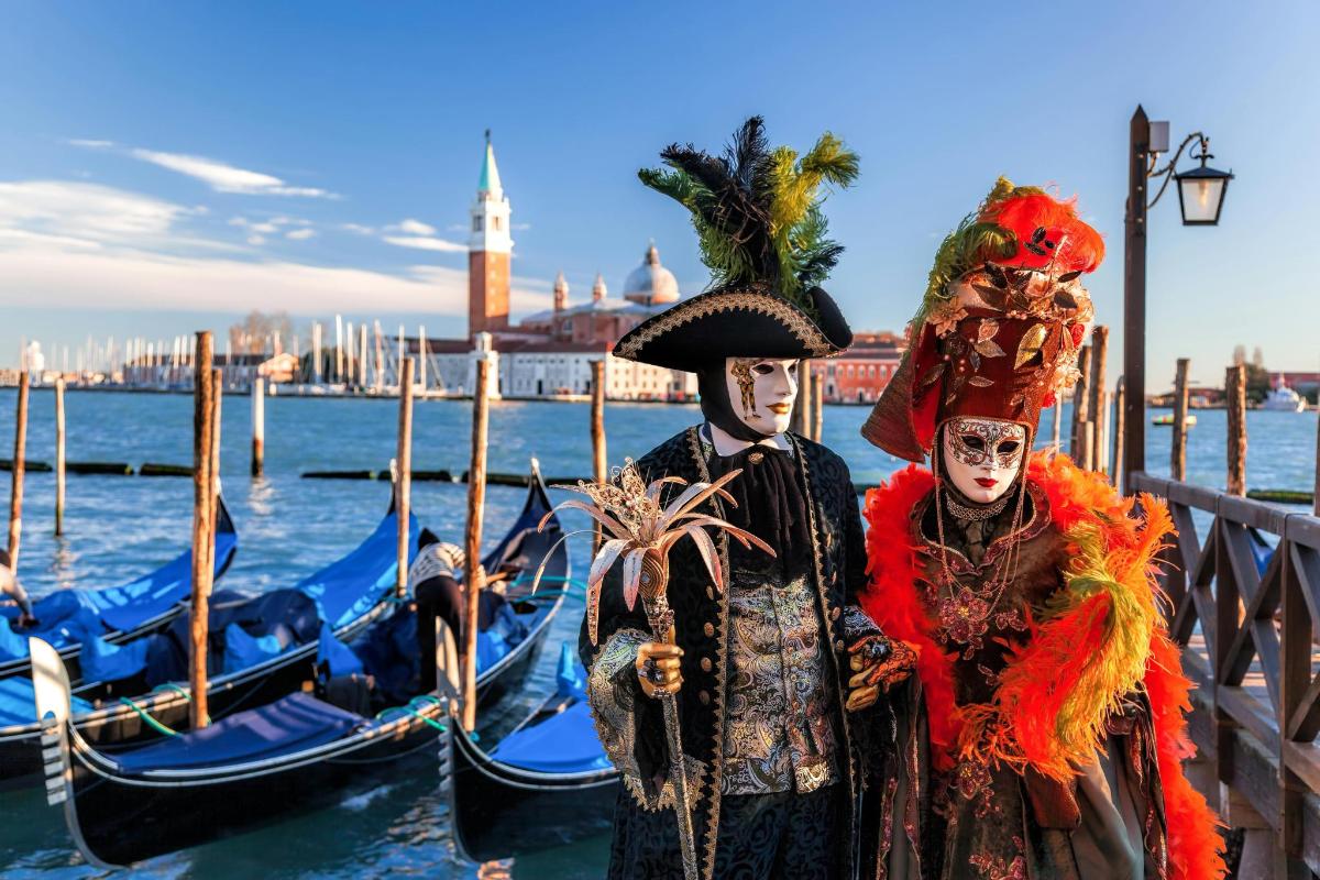 due persone vestite in costume in piedi vicino all'acqua con le gondole