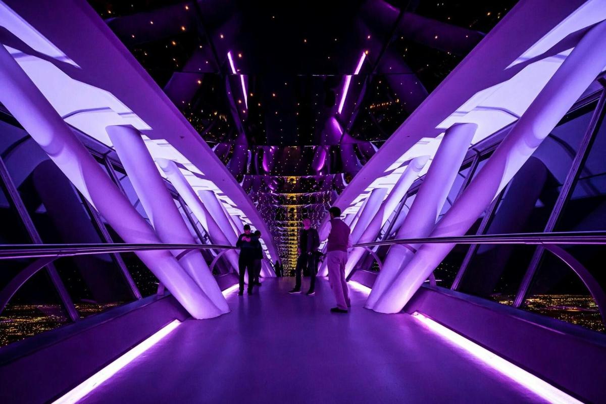 un grup de persones caminant per un pont amb il·luminació morada