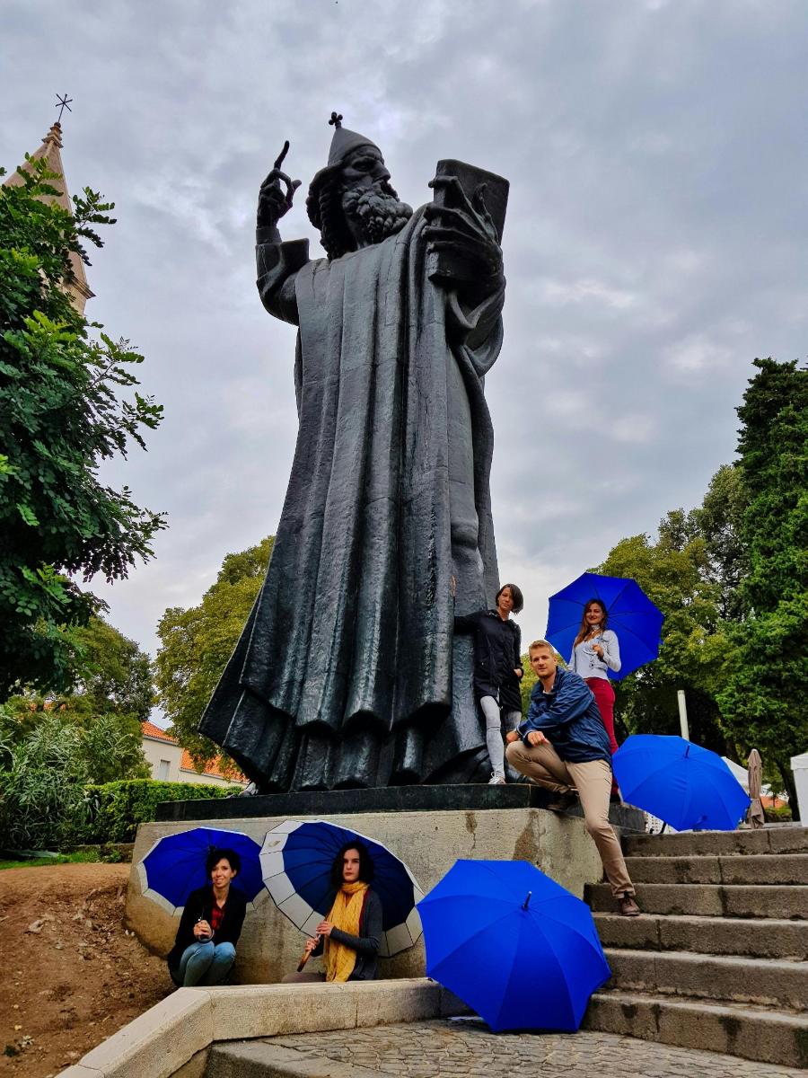 eine Gruppe von Menschen, die mit Regenschirmen um eine Statue herum sitzen