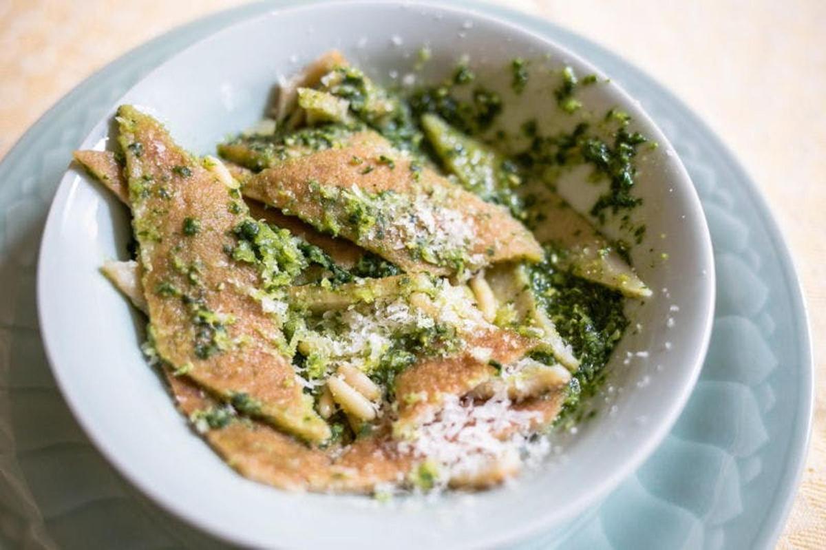 uma tigela branca de comida com pesto e macarrão