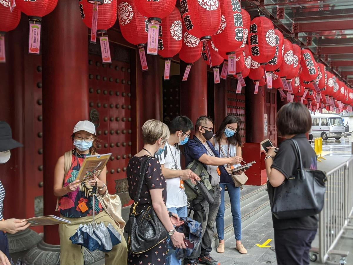 people wearing face masks stand outside a building with red lanterns