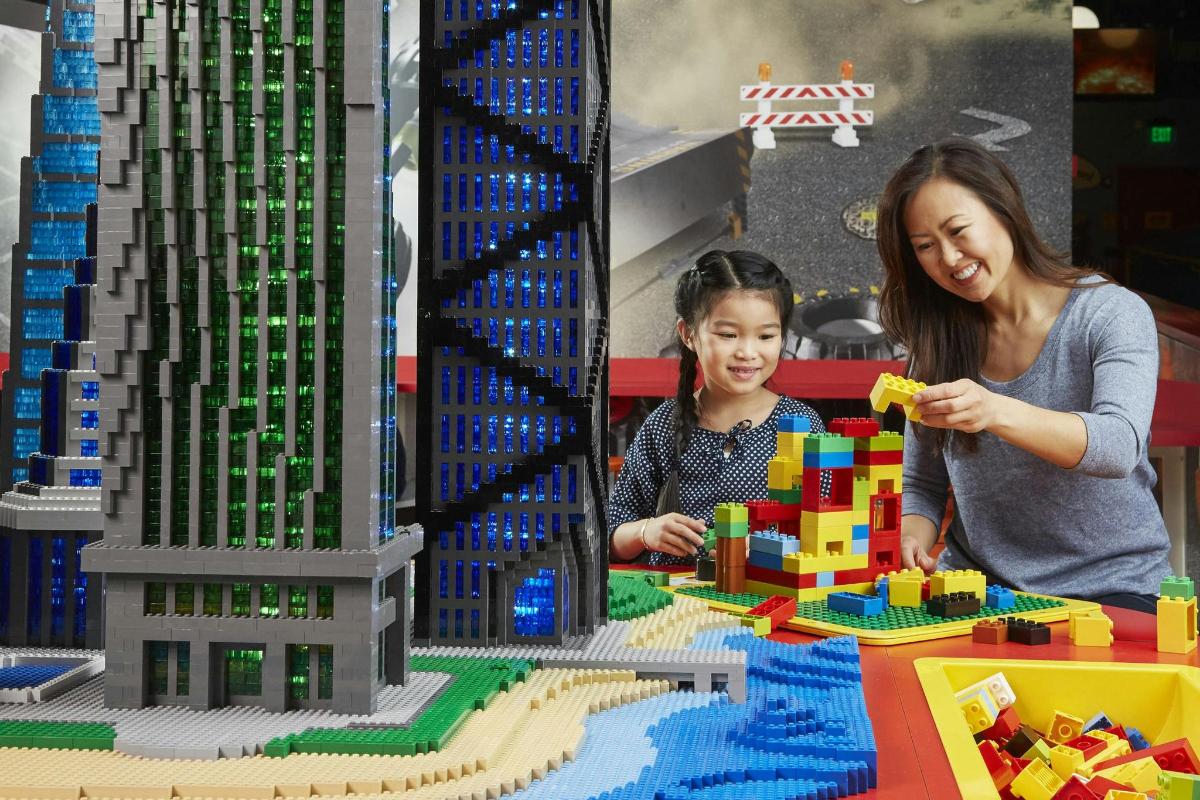 naine ja laps mängivad linna lego mudeliga