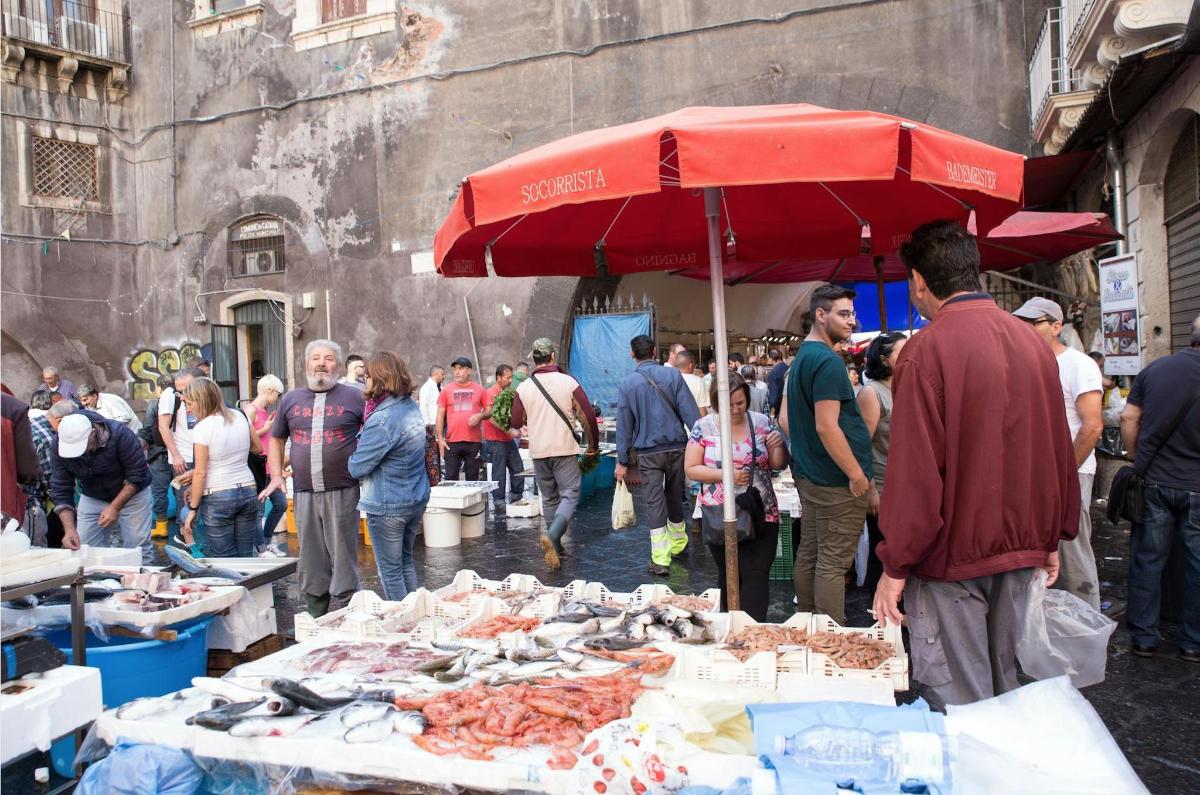 skupina ljudi, ki stojijo okoli tržnice z rdečim dežnikom