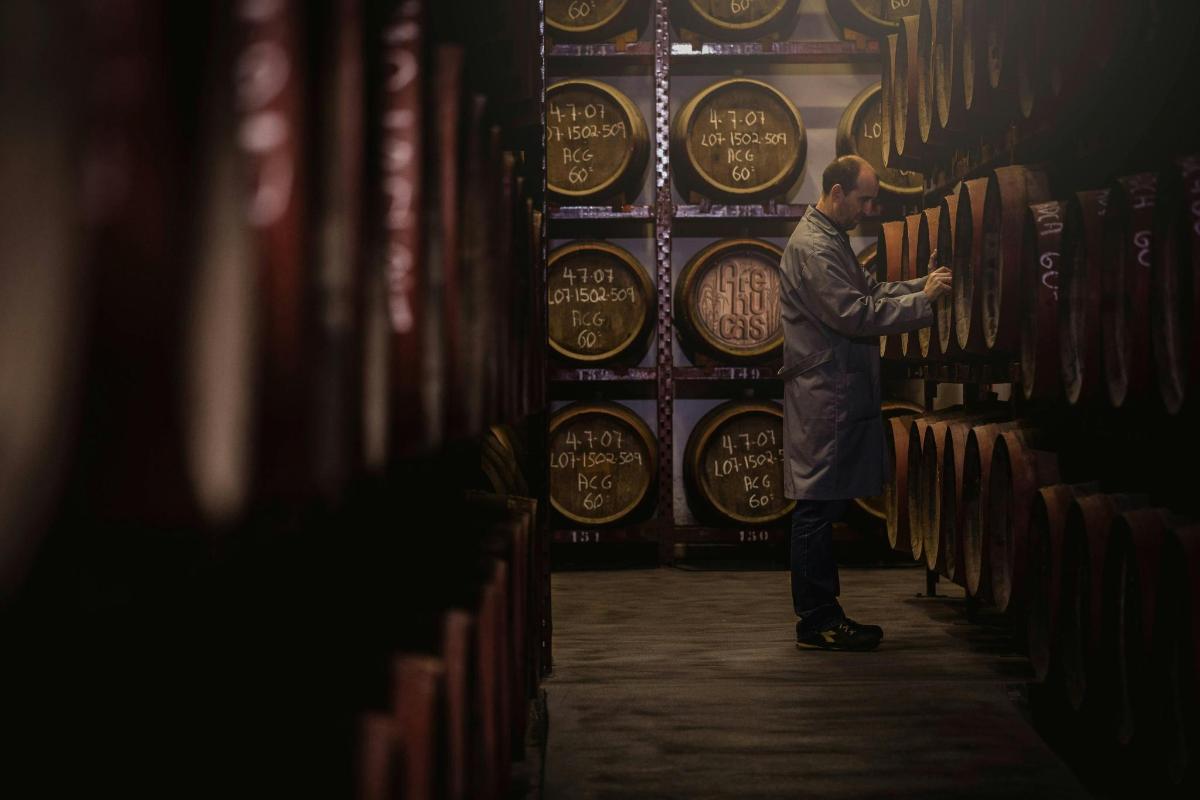 un uomo in piedi davanti a un muro di botti di vino