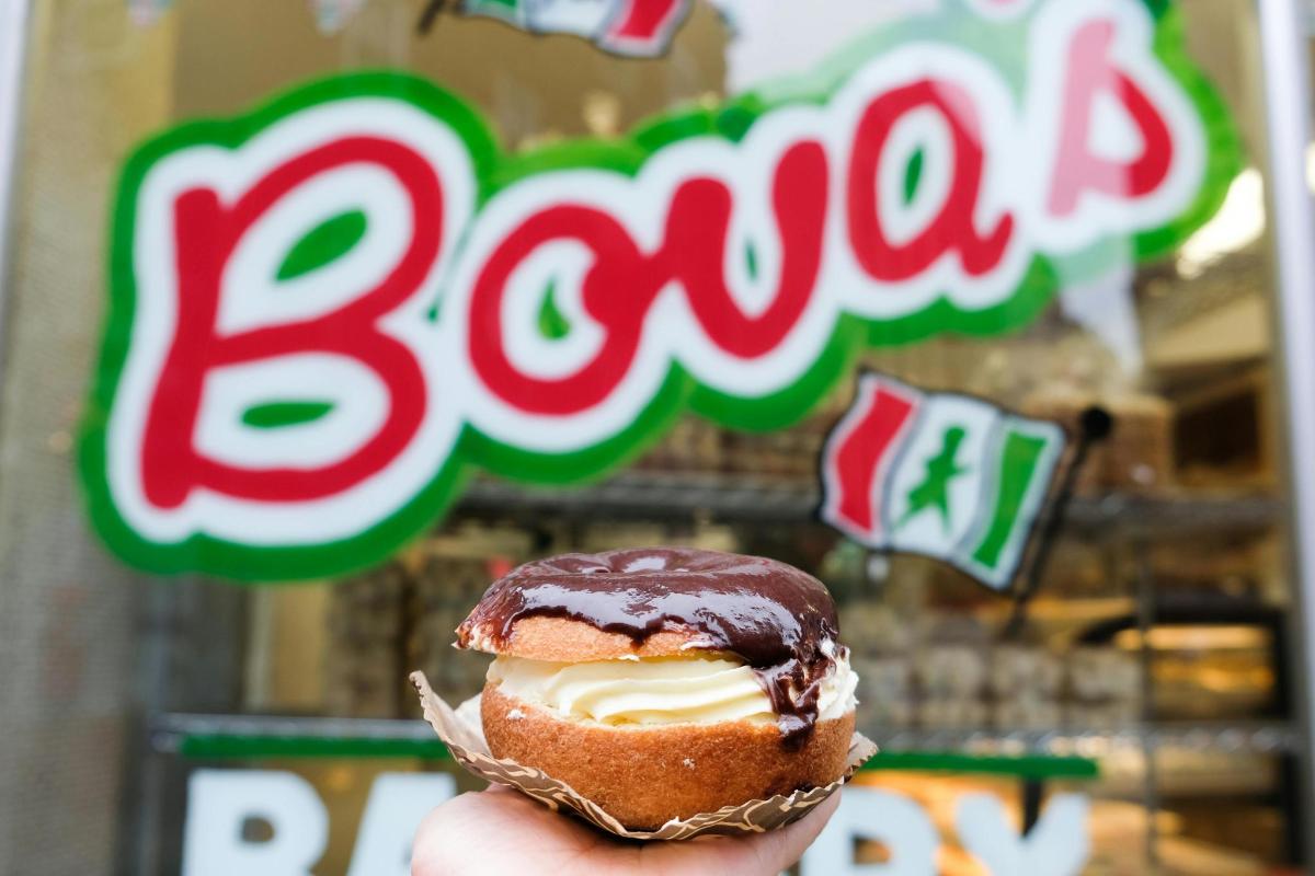 a person holding a pastry in front of a store