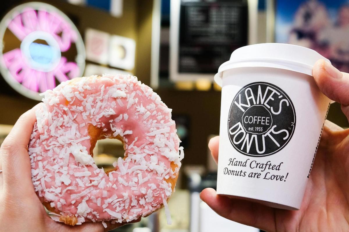 a person holding a pink doughnut and a cup of coffee