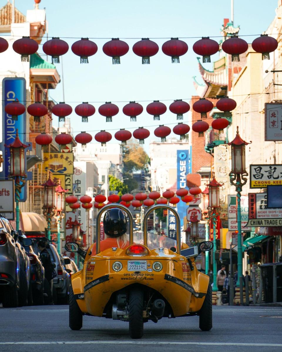 a yellow car driving down a city street with umbrellas