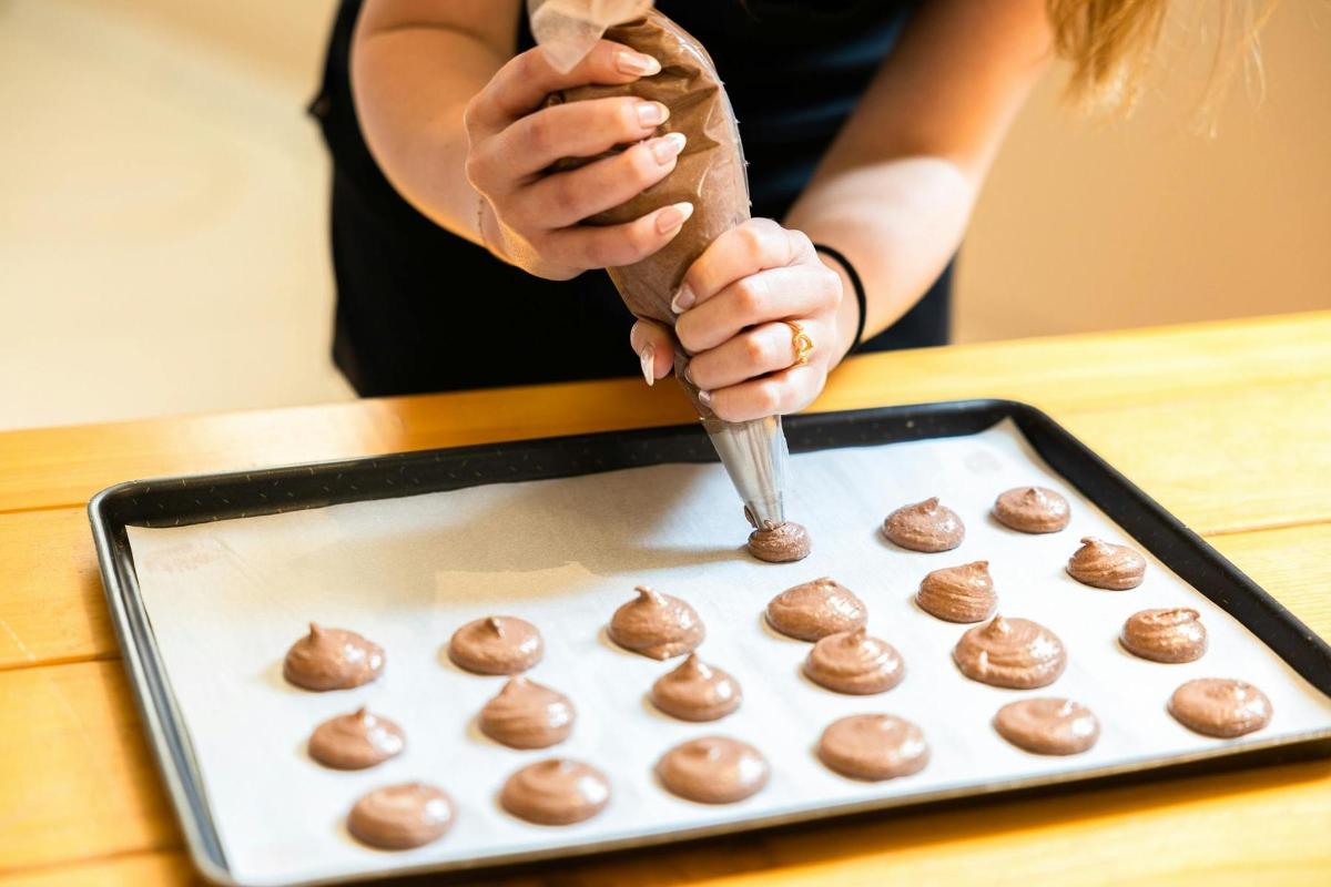 a woman is using a spoon to make chocolate covered donuts