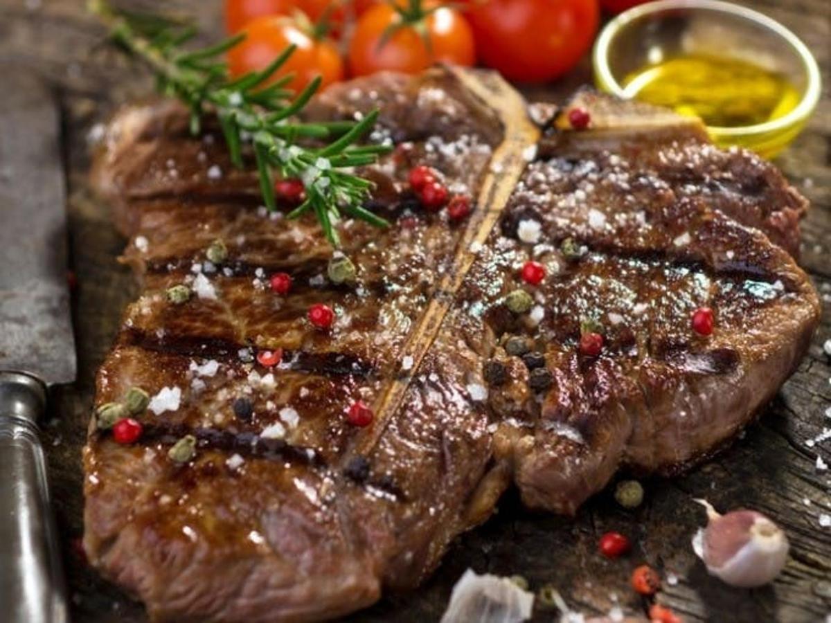 Un bistec en una mesa con tomates encima.