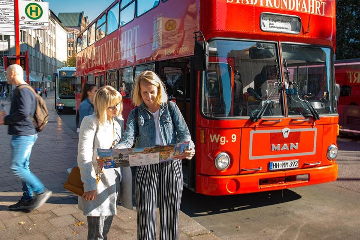 two women holding a map in front of a double decker bus