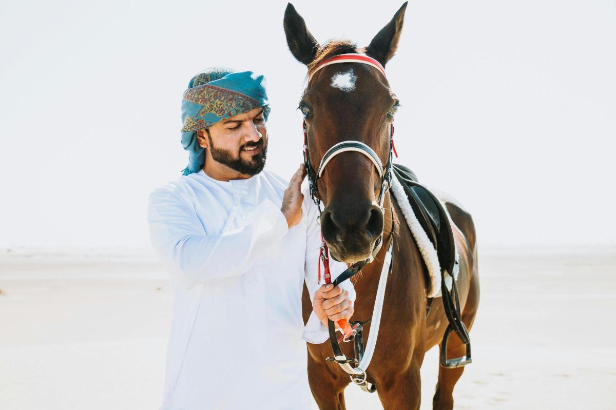 a man standing next to a horse on the beach