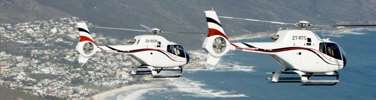 два білі гелікоптери летять над водою