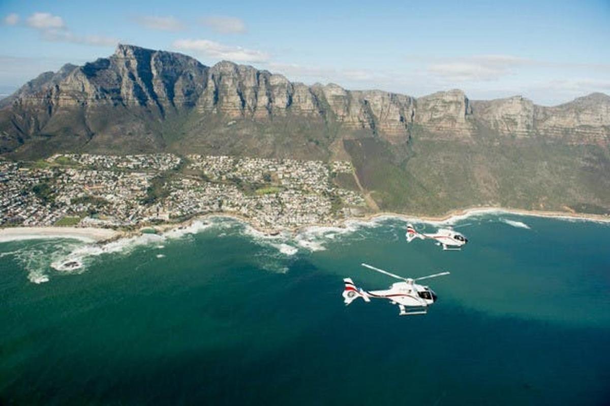 dois helicópteros voando sobre a água perto de uma montanha