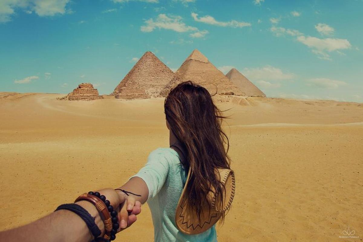 um homem e uma mulher de mãos dadas em frente às pirâmides