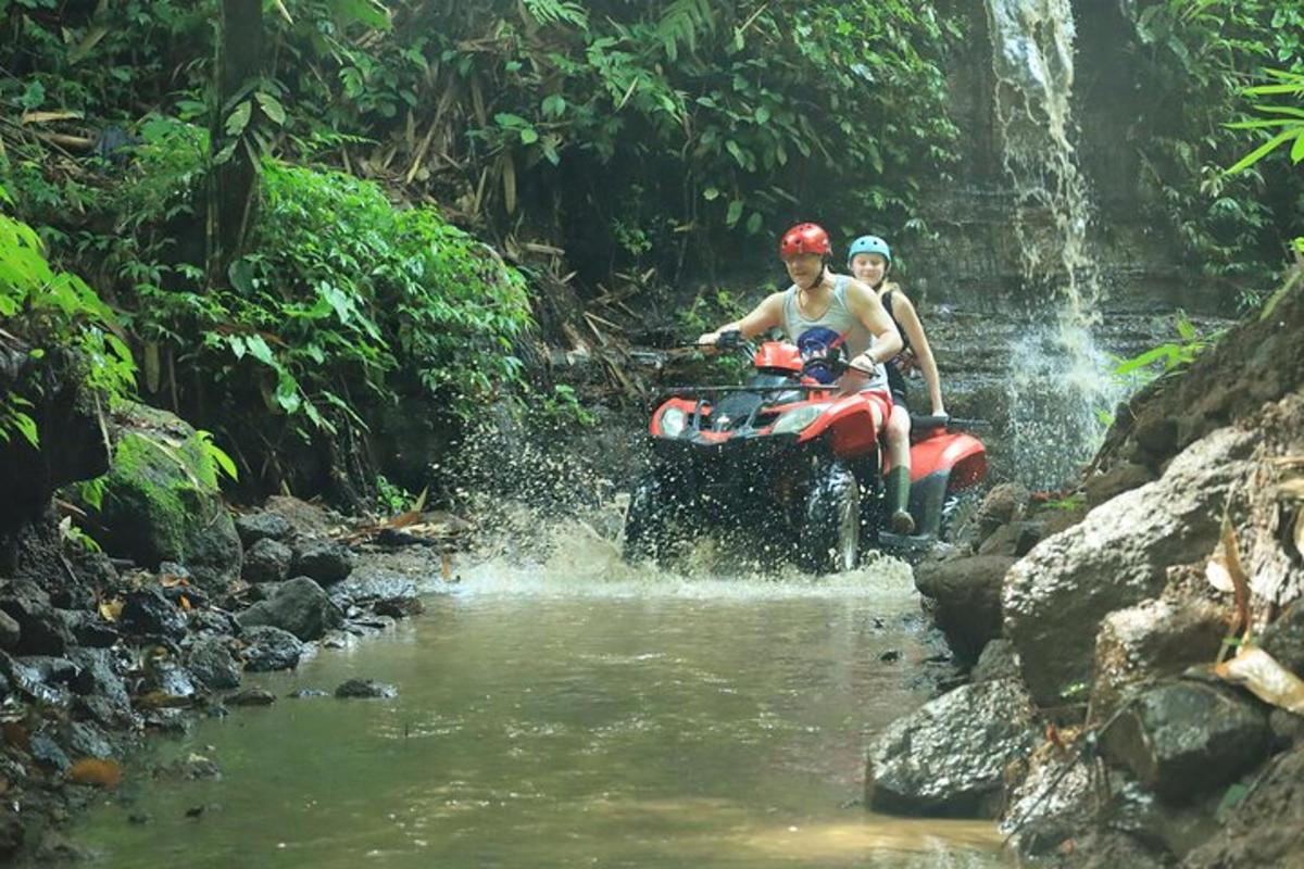 duas pessoas em um quadriciclo atravessando um riacho em uma cachoeira