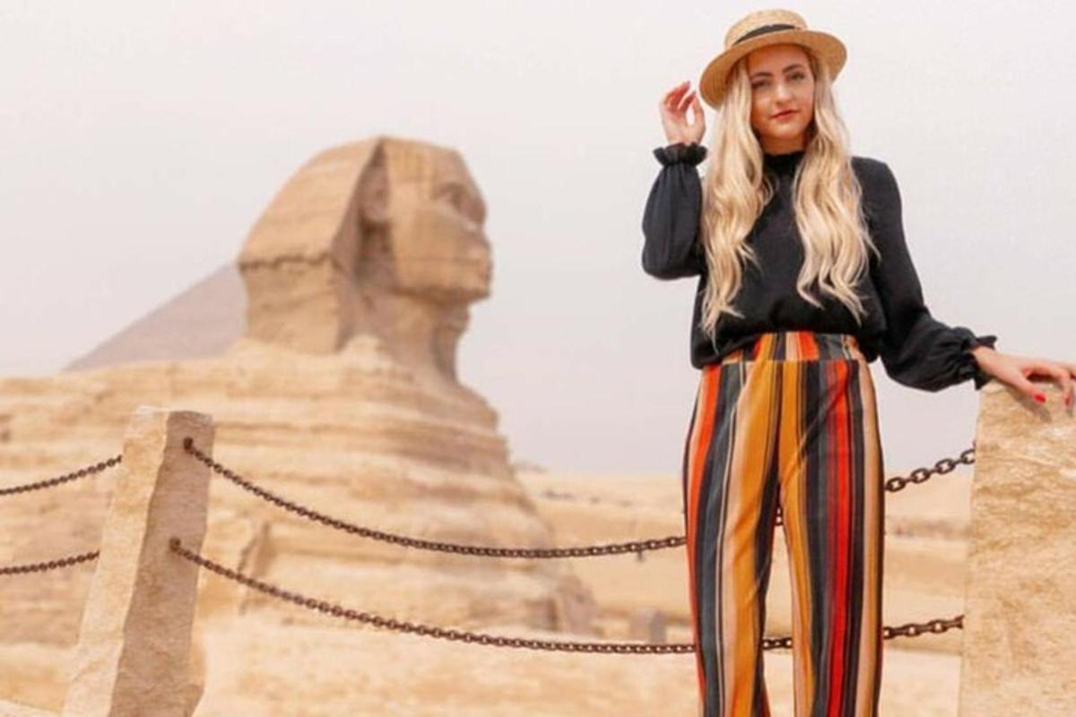 een vrouw met een hoed die voor de piramide staat