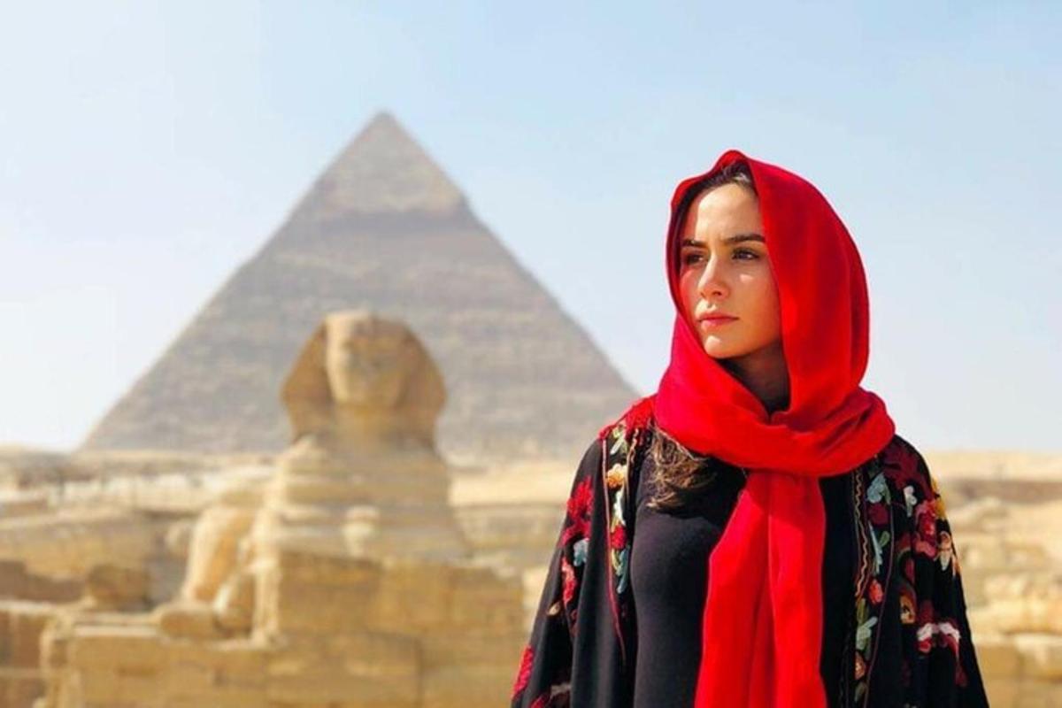 een vrouw met een rode hijab die voor de piramides staat
