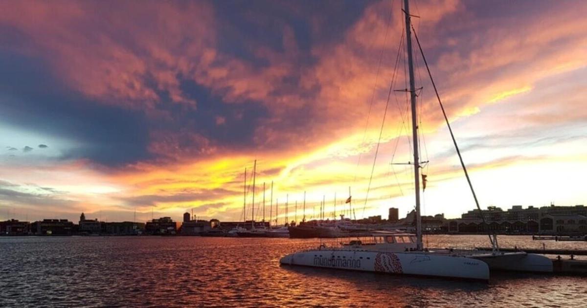a sail boat docked in a harbor with a sunset